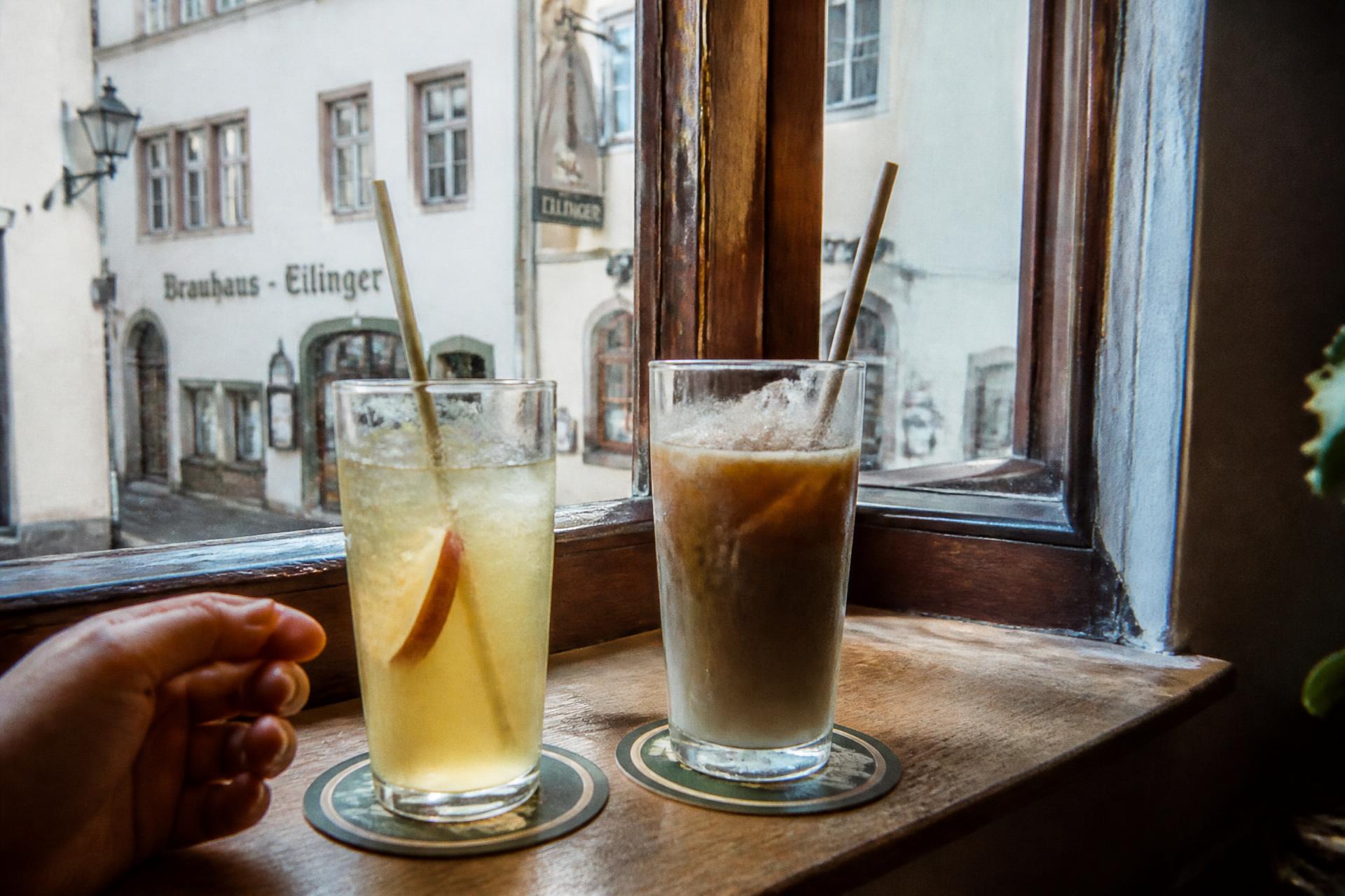 Zwei kalte Getränke mit Strohhalm auf einem Fensterbrett, draußen die Altstadtgasse